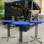 Katettu esiintymislava, äänentoistotekniikka ja siniset pystypöydät ulkoilmatapahtumassa – Vuokrausfirma